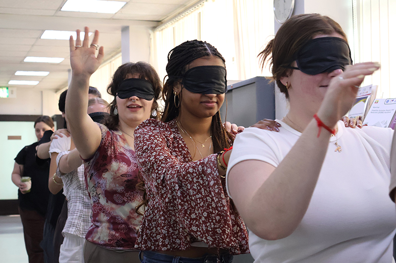 Students roll play on empathy exercise; they put on blindfold to demonstrate as a blind person. 